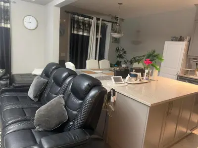 a living room with a black leather couch and a counter at Spacious Bedroom-Near Airport YYC in Airdrie
