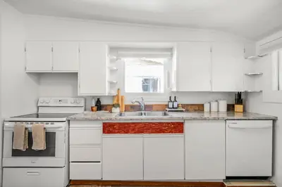 a white kitchen with white cabinets and a sink at The Red Steps Away From World's Largest Dinosaur 3BR House in Drumheller