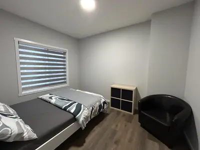 a bedroom with a bed and a chair and a window at 1-bedroom private suite, 20 minutes from the airport, with a kitchen in Edmonton