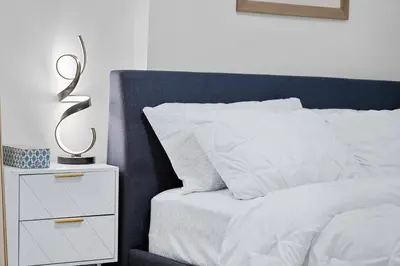 a bedroom with a white bed with a nightstand with a statue on it at Cozy 2BR Suite with Kitchen, AC Near U of C, Winsport, Banff and Hospitals in Calgary