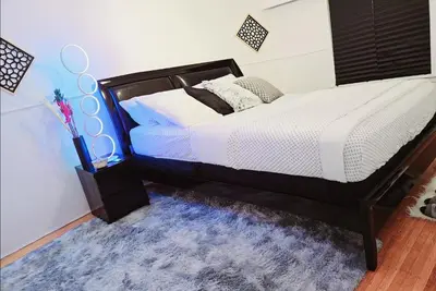 a bedroom with a black bed with a blue rug at Private 2 BR Cozy Home Private Parking Free Sparkling and Goodies! 4 mins from Metrotown in Burnaby