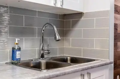 a stainless steel sink in a kitchen with gray tiles at Cozy & Spacious 2BR in Downtown very close to Stampede and 17th Ave with Parking and AC in Calgary