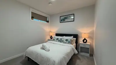 a white bedroom with a bed and two lamps at Cozy & Quiet Calgary 2BR Suite in Calgary