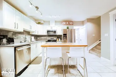 a kitchen with white cabinets and a island with stools at Chic Retreat with Hot Tub - King Bed - Fireplace - WEM in Edmonton