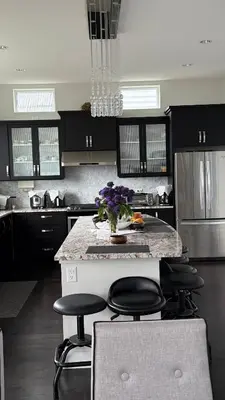 a kitchen with a counter with stools and a vase with purple flowers at Carrie The Gentle Nest 1 in Coquitlam