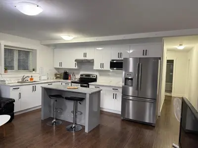 a kitchen with white cabinets and a stainless steel refrigerator at Private two bedroom basement suite Sleeps six people in Surrey