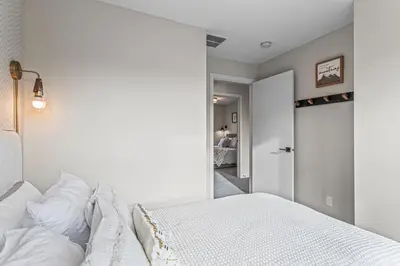 a white bedroom with a bed and a hallway at Peak n Plunge Insane MTN View Pool n Hot Tub K201 in Canmore