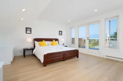 a white bedroom with a large bed with yellow pillows at Elegant Spanish Villa with Ocean & Mountain Views in Vancouver