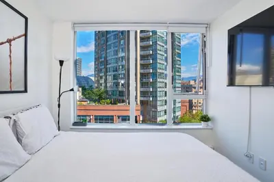 a bedroom with a white bed and a large window at Cozy Urban Living! 2 mins from BC place, private parking ! in Vancouver