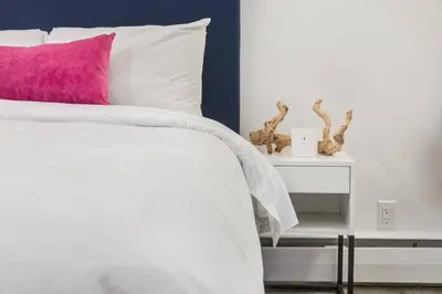 a white bed with a pink pillow and a side table at Gateway Suites Private Double room near Banff in Canmore