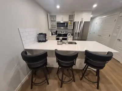 a kitchen with a large white counter with four bar stools at Superb 1-Bdr Apt in New Condo in Calgary