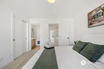 a white bedroom with a large bed with a green rug at Modern Luxury Townhome near Aspen Landing and Winsport in Calgary