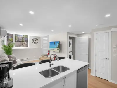 a white kitchen with a sink and a living room at Exquisite 1-Bdr Condo Apt in Calgary