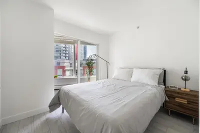 a white bedroom with a bed and a window at Modern Condo in Downtown Vancouver in Vancouver