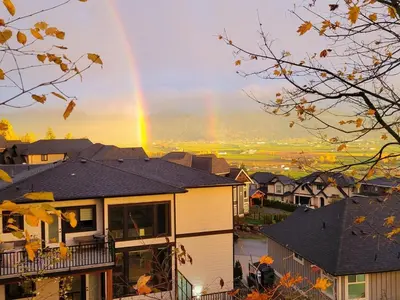 a rainbow in the sky over houses andyards at Beautiful Mountain Retreat with a View in Abbotsford
