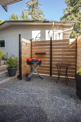 a backyard with a fence and a grill and a table at Modern Lynn Valley Retreat with Mountain and City Views in North Vancouver
