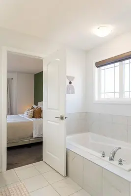a white bathroom with a tub and a bed at Spacious Suite in Calgary