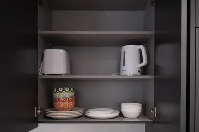 a cupboard with plates and a toaster and cups at Brand New Cozy Suite near Collingwood School in West Vancouver