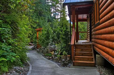 a porch of a cabin with a staircase next to a house at Wild Renfrew Seaside Cottages in Port Renfrew