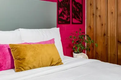 a bed with a yellow pillow and a pink wall at Gateway Suites Sweet Getaway near Canmore and Banff in Canmore