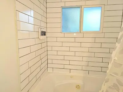 a white tiled bathroom with a tub and a window at Kirvia's retreat 