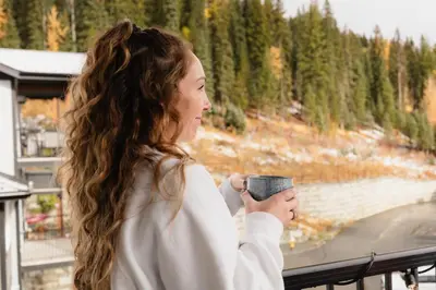 a woman holding a cup of coffee on a balcony at The Après Arcade in Sun Peaks