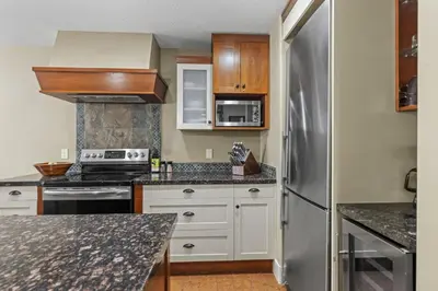 a kitchen with white cabinets and a stainless steel refrigerator at Mountain View Escape Sleeps 6 with Hot Tub and Pool in Canmore