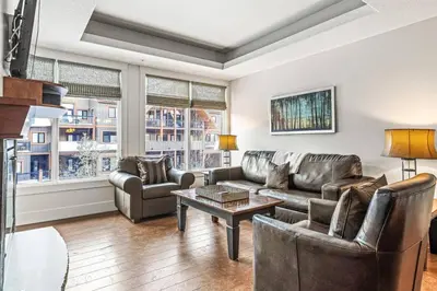a living room with leather furniture and windows at Mountain View 2BR Condo with Hot Tub, Pool and Gym in Canmore
