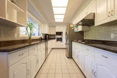 a large kitchen with white cabinets and a refrigerator at South Vancouver Garden Home in Vancouver