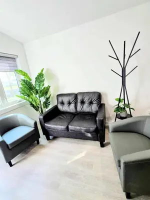 a living room with a black leather couch and a plant at The Oasis in Stettler in Stettler