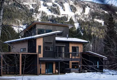 a log house with snow on a mountain at CAPOW House in Revelstoke