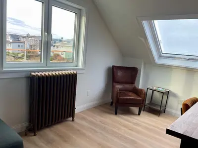 a room with a chair and a radiator and two windows at The Golden Sky Sanctuary at the Algonquin Residence in Prince Rupert