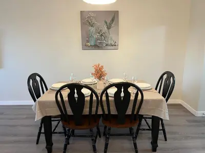 a dining room table with four chairs and a painting at 3 Adjacent 4-bed Homes - Park Views, Fully Stocked in Grande Prairie