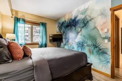 a bedroom with a bed with a painting on the wall at 3BR Rockies Condo Heated Pool and Hot Tub in Canmore