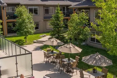 a patio with tables and umbrellas in front of a building at Cozy Condo With Hot Tub Gym and Underground Parking in Dead Man's Flats
