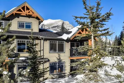 a house in the snow with a mountain at Cozy Condo With Hot Tub Gym and Underground Parking in Dead Man's Flats