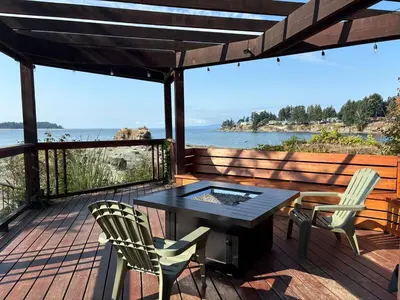 a deck with a table and chairs and a view of the water at Oceanside Getaway in Nanoose Bay