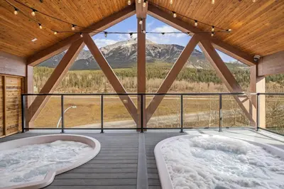 two tubs on a deck with a view of a mountain at Brand New 1BR Canmore Retreat Hot Tub, Sauna, Gym in Canmore