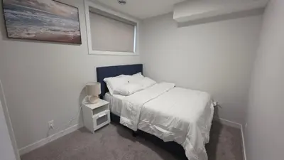 a white bedroom with a bed and a night stand at Modern 2BR Suite in Seton, Calgary in Calgary