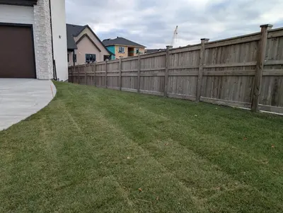 a backyard with a wooden fence and a green yard at 21 Greenwich Common NW Calgary Alberta in Calgary