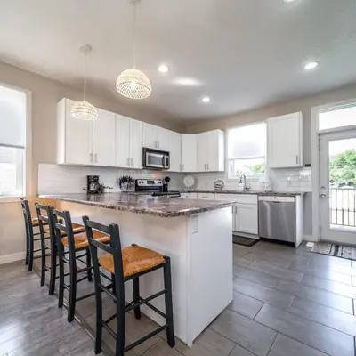 a kitchen with white cabinets and a bar with chairs at BoHo House-Sleeps 17-Garage-3 Kitchens-Fireplace in Edmonton