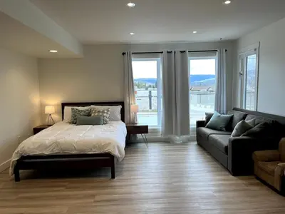 a bedroom with a bed and a couch and windows at Camelia Home in Kelowna