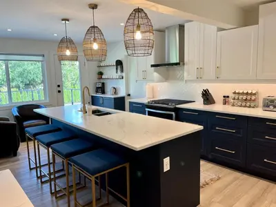 a kitchen with white cabinets and a blue island with bar stools at Camelia Home in Kelowna