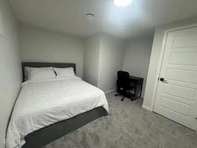 a bedroom with a white bed and a black chair at Rockies Golden Retreat 2BR Suite at Glacier Ridge NW Calgary in Calgary