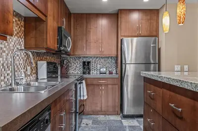 a kitchen with wooden cabinets and a stainless steel refrigerator at Stunning Condo - Hot Tubs & Steam Room - Pets Ok in Canmore
