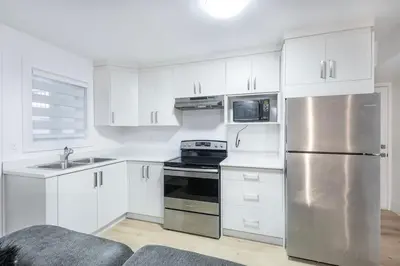 a kitchen with white cabinets and a stainless steel refrigerator at Bright & Modern Surrey Basement Suite with Queen Beds & Parking in Surrey