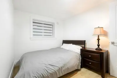 a bedroom with a bed and a lamp and a window at Bright & Modern Surrey Basement Suite with Queen Beds & Parking in Surrey