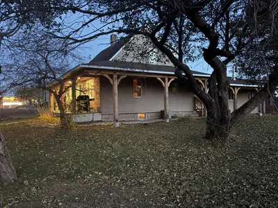 a white house with a black roof and a tree at maison de la Ferme in Bélanger