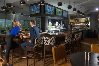 a couple sitting at a bar in a restaurant at Applause Hotel Calgary Airport by CLIQUE in Calgary