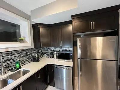 a kitchen with brown cabinets and a stainless steel refrigerator at Cozy 2BR Retreat | Edmonton SW | Smart TV + Wi-Fi in Edmonton